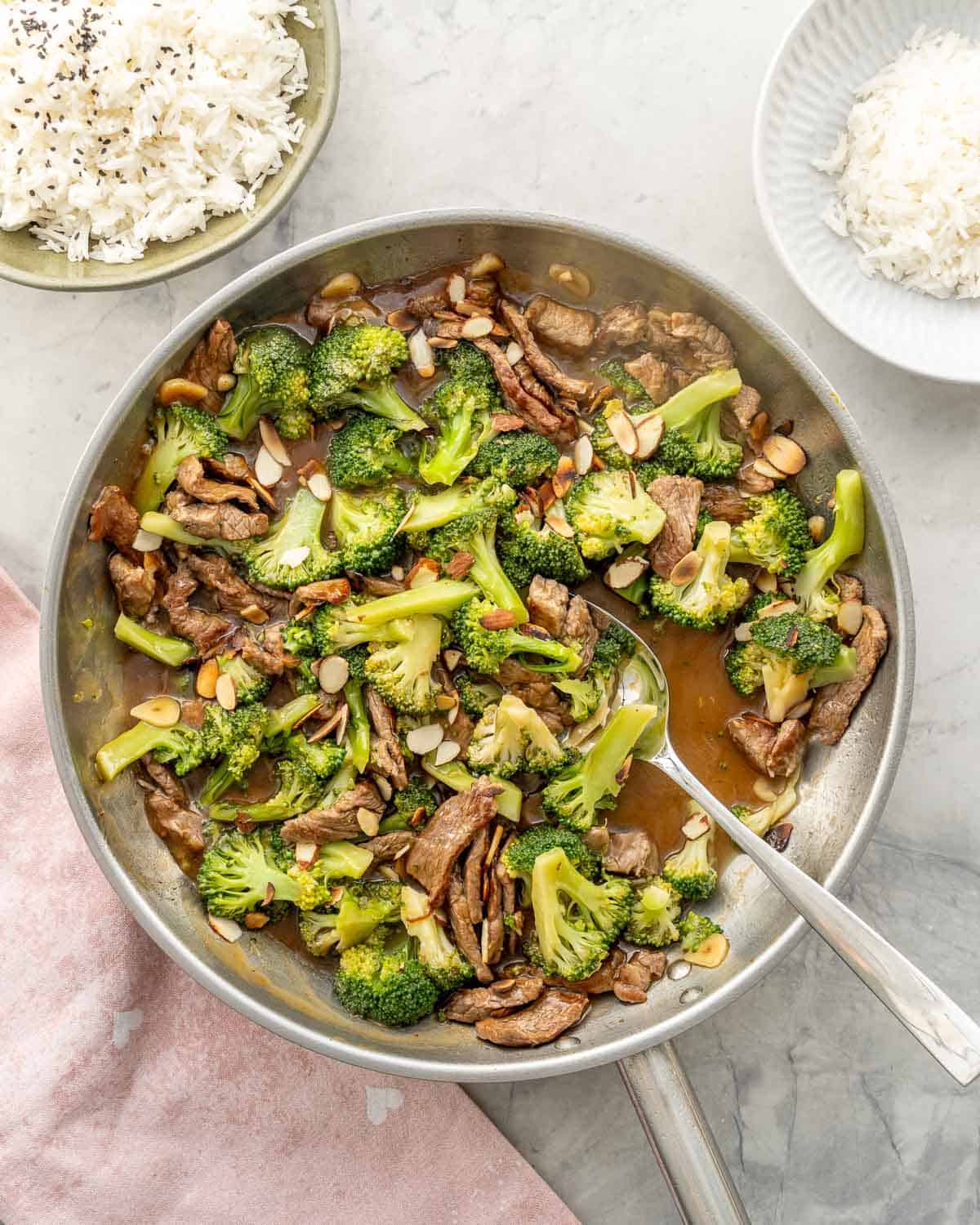 Beef and broccoli stir fry in pan with spoon ready to serve, chopped almonds garnished on top.