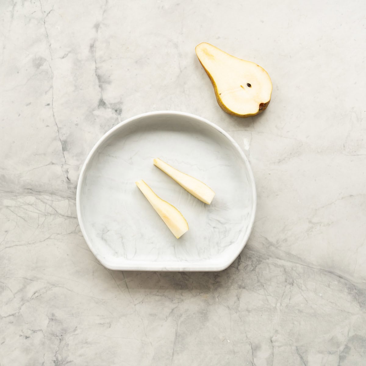 2 buttons of ripe pear with skin on on a marbled baby plate.