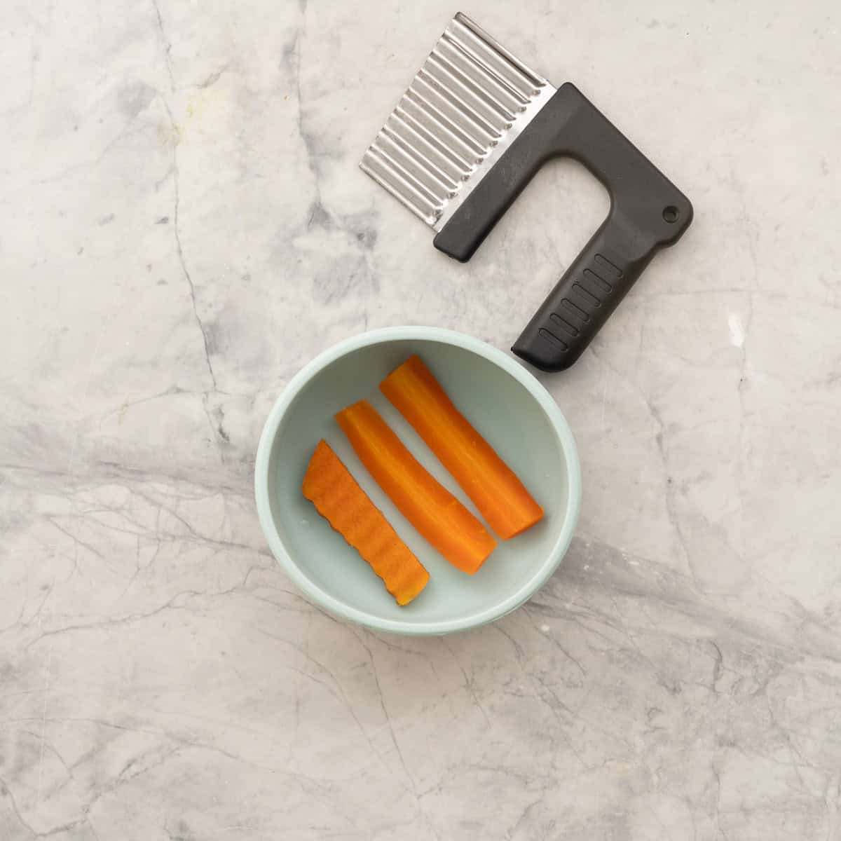 Three wedges of carrot, once cut with crinkle cutter. In baby silicone bowl on bench top.