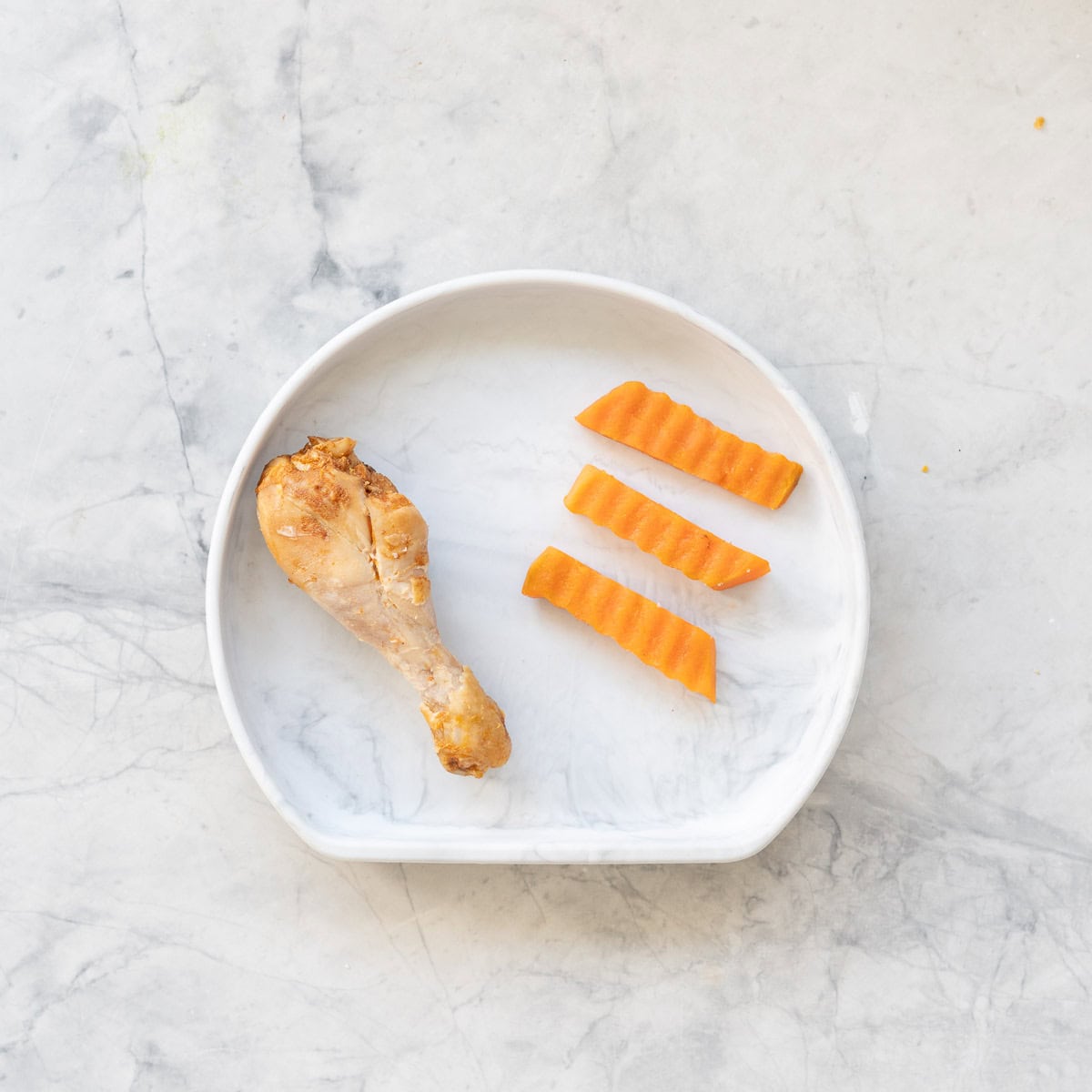 Cooked chicken drumstick, three pieces of cooked kumara cut by crinkle cutters on baby silicone plate.