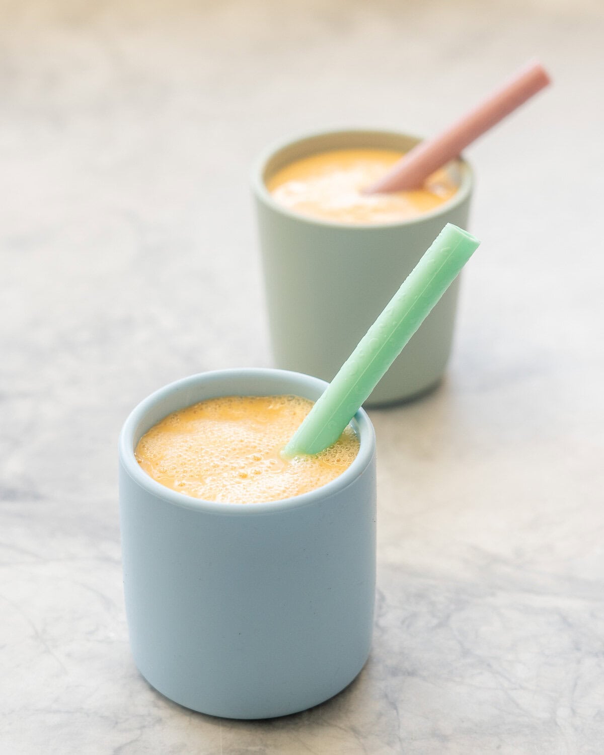 Vibrant orange carrot smoothie in pastel blue and green silicone children cups with silicone colourful straws.