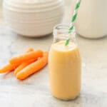 Carrot smoothie in small glass drinking jar with straw.