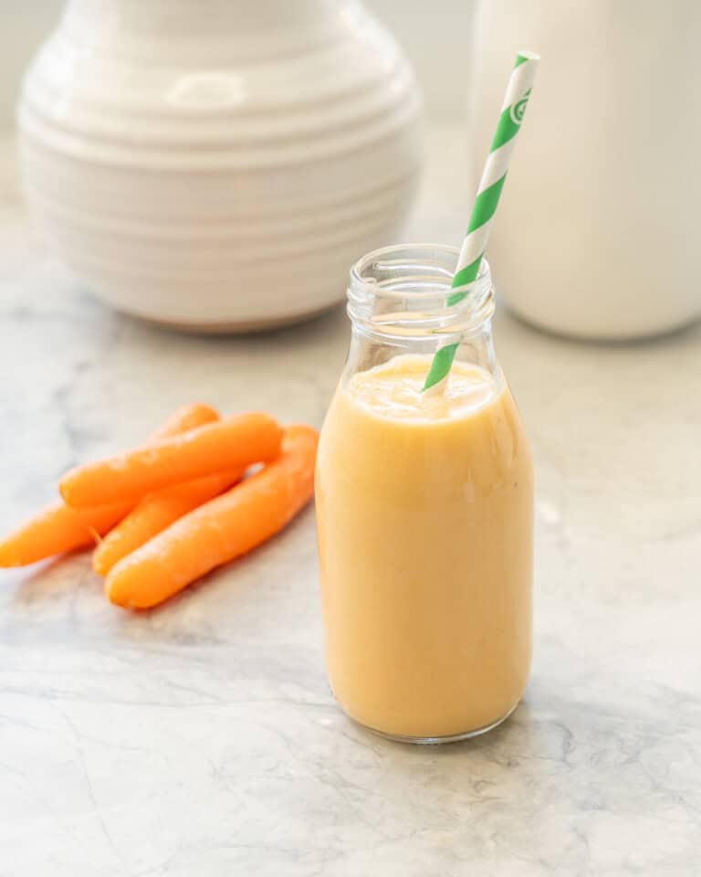 Carrot smoothie in small glass drinking jar with straw.