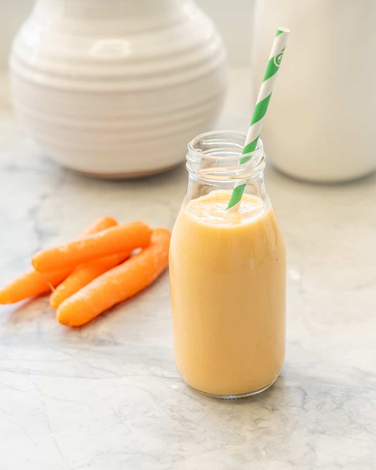 Carrot smoothie in small glass drinking jar with straw.