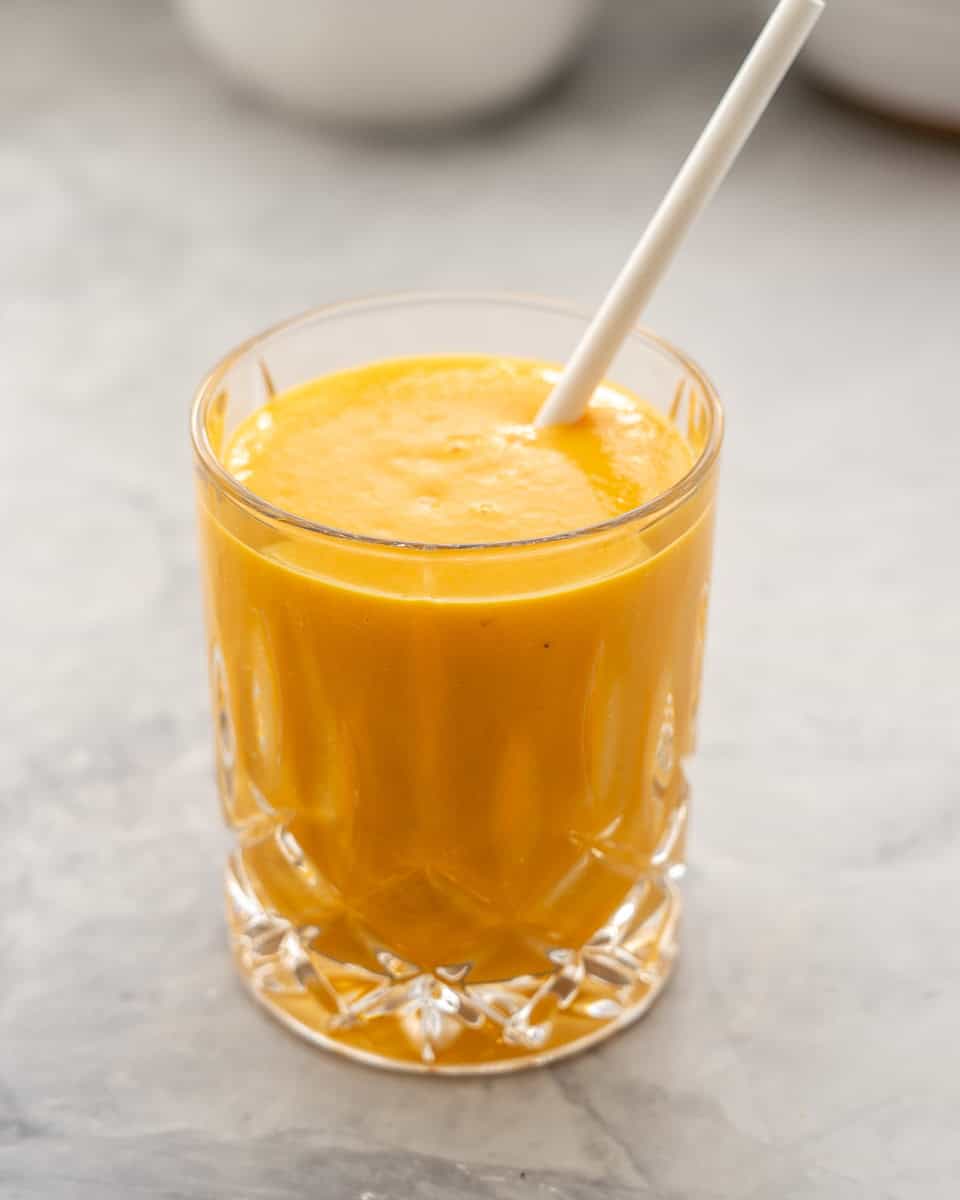 Carrot smoothie filled to the top of glass with straw in it.