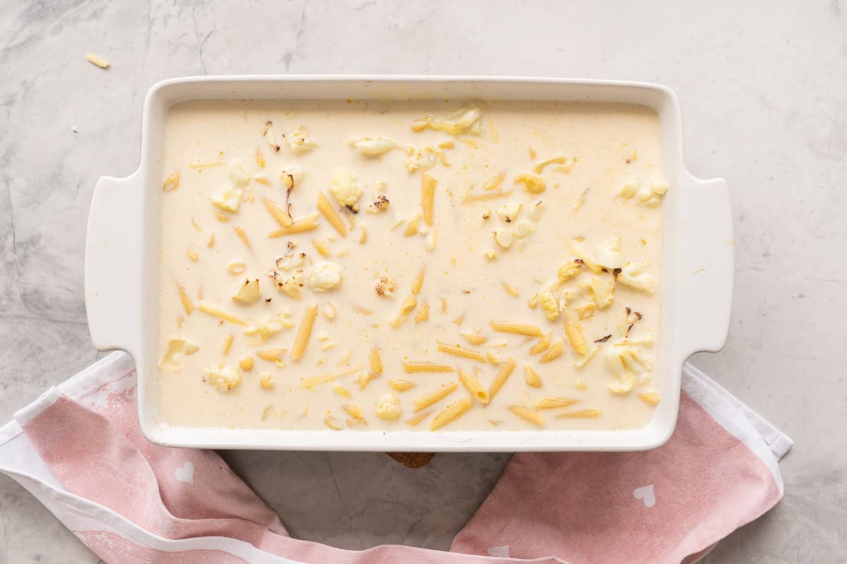 Cauliflower pasta bake with all ingredients in baking dish and milk mixture poured over the top.