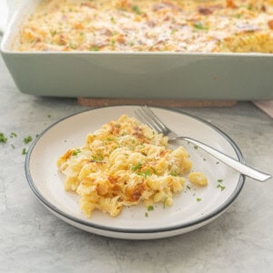 Serving of cauliflower bake on plate with fork on bench top with baking dish in background.