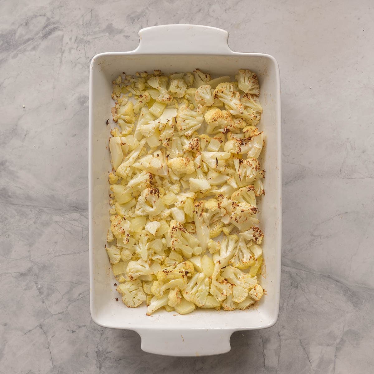 Onion and Cauliflower placed on the bottom of baking dish on bench top.