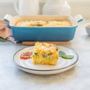 A piece of hash brown egg bake served on a plate with chutney, baking dish with remaining blurred in background.