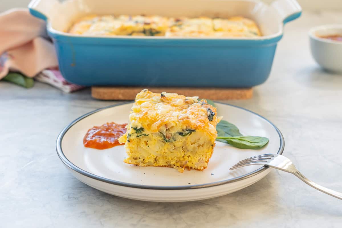 A piece of hash brown egg bake served on a plate with chutney, baking dish with remaining blurred in background.