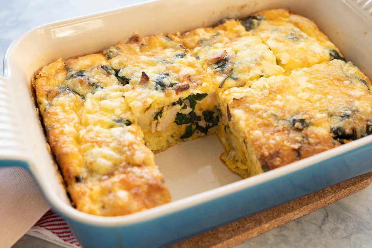 A baking dish of cooked hash brown egg bake with a portion removed so you can see the layers of ingredients.