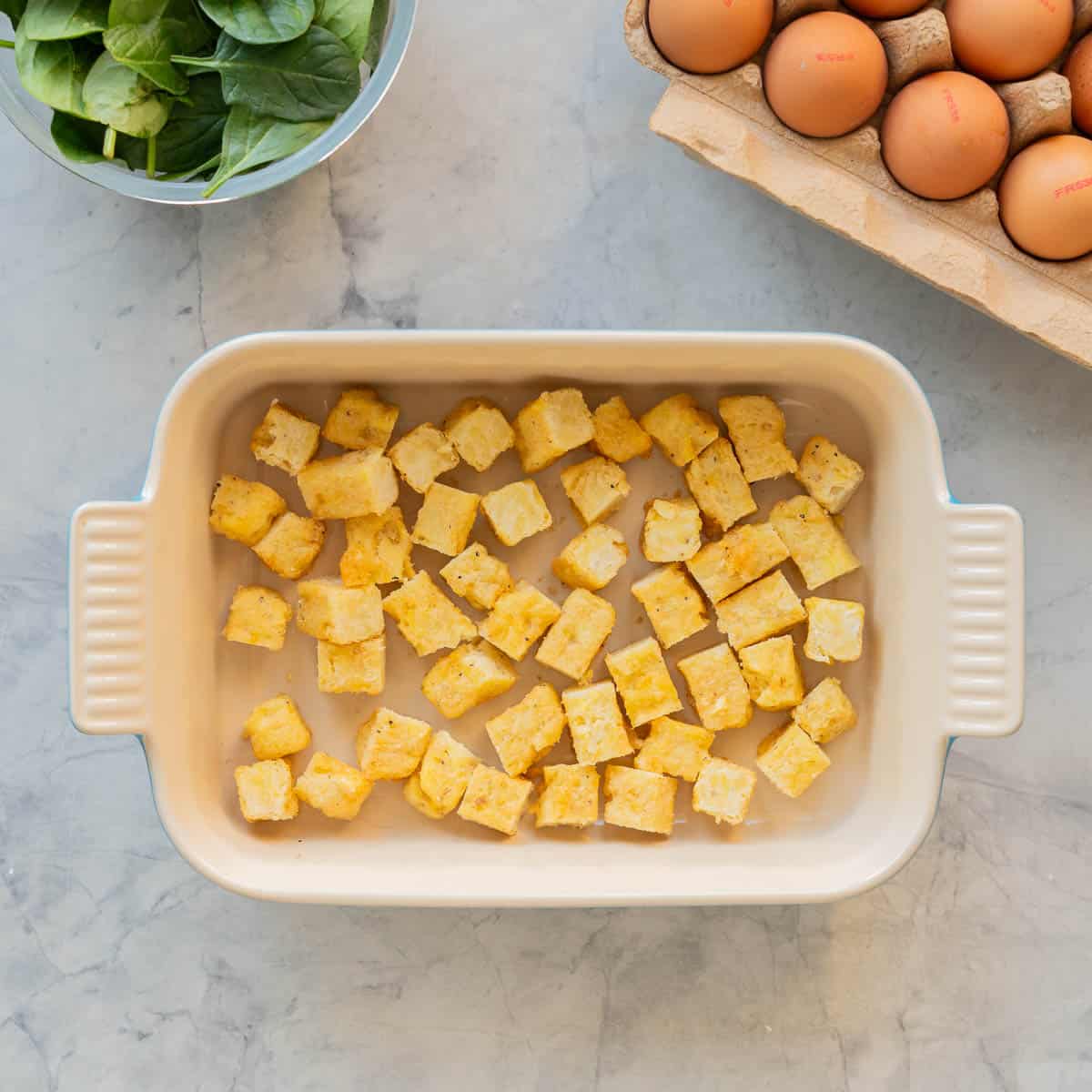 Cubed hash brown pieces in the bottom of an baking dish.