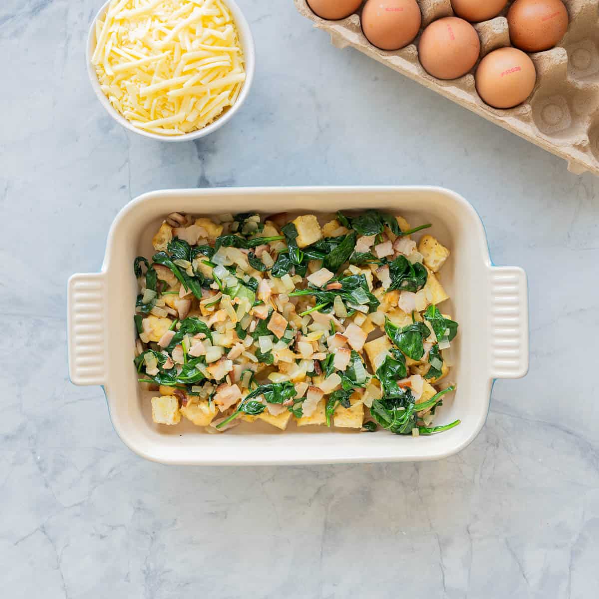 Spinach, bacon and onion placed on top of the cubed hash browns in baking dish.