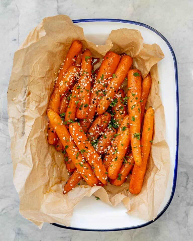 Glazed carrots roasted and placed on brown baking paper in serving dish, garnished with sesame seeds and chopped parsley.