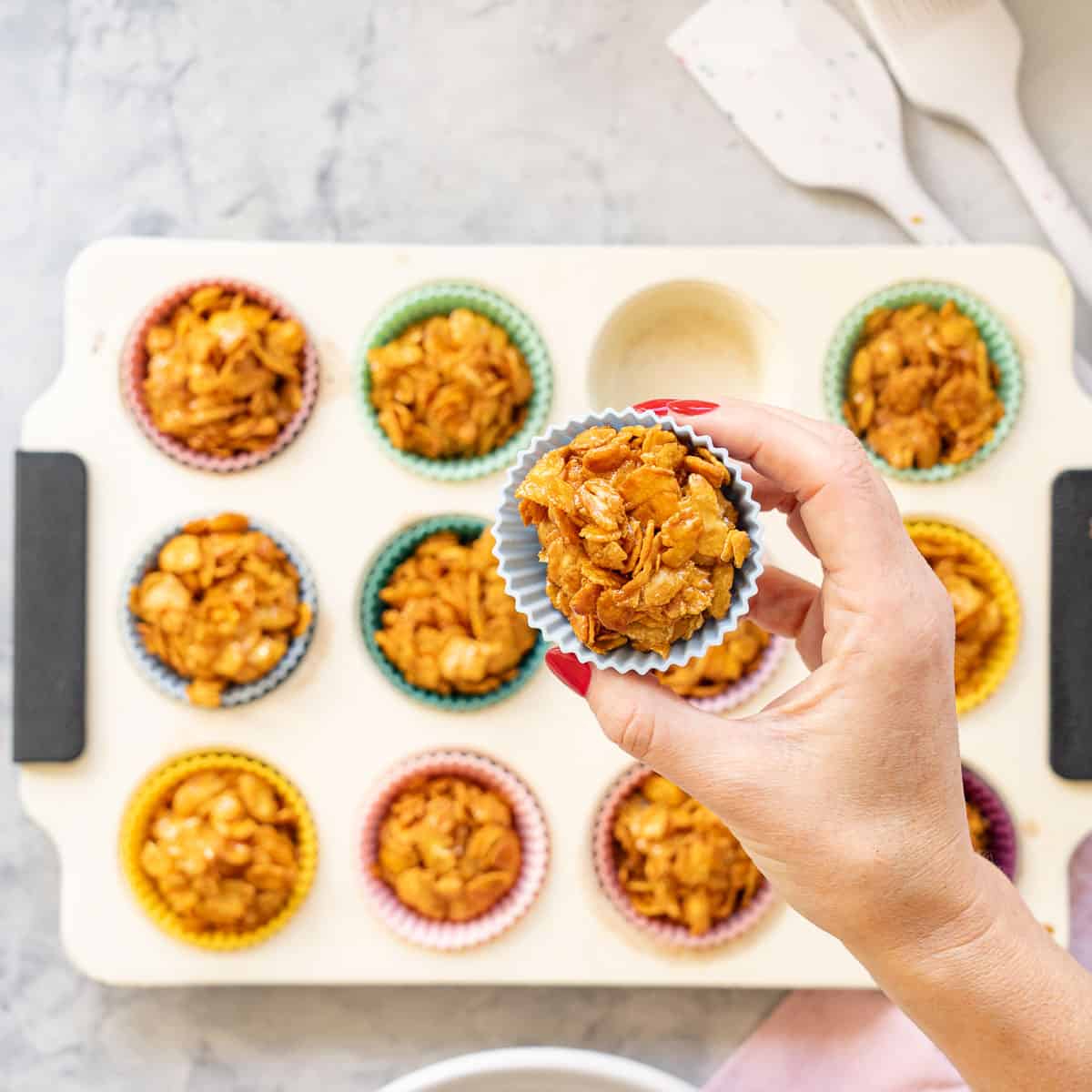 A honey joy being held above a muffin tray of more.