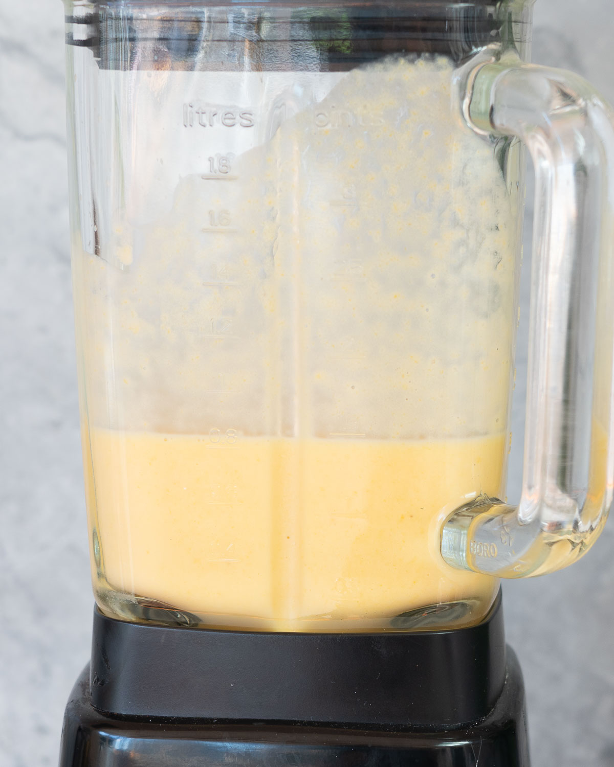 A blender jug one third fill of peach coloured smoothie. 