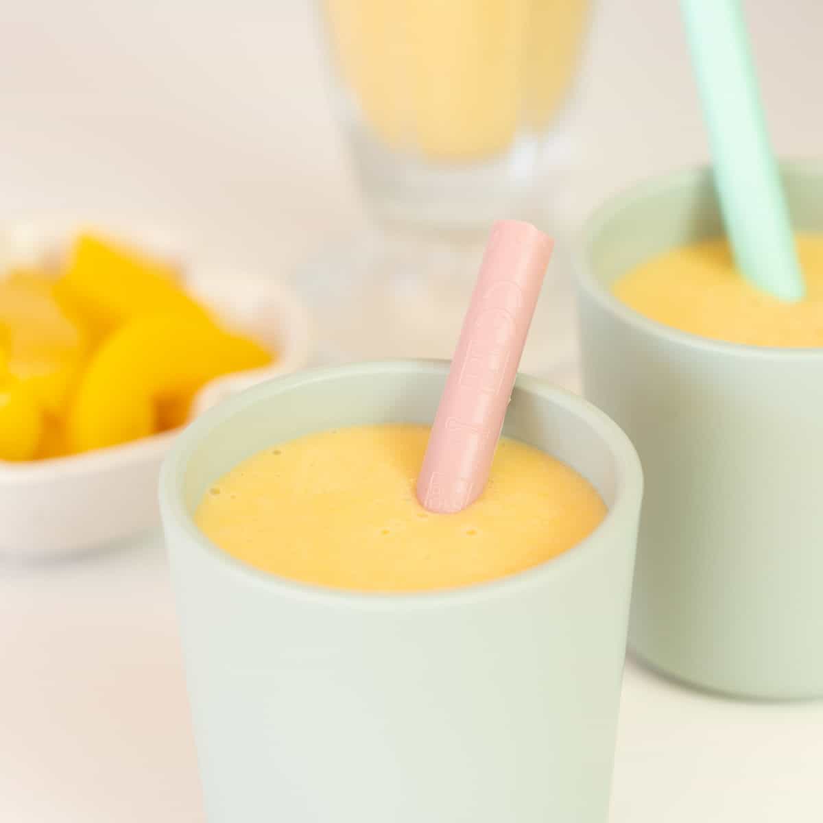 Close up of the top of a green toddler cup filled with peach coloured smoothie. 