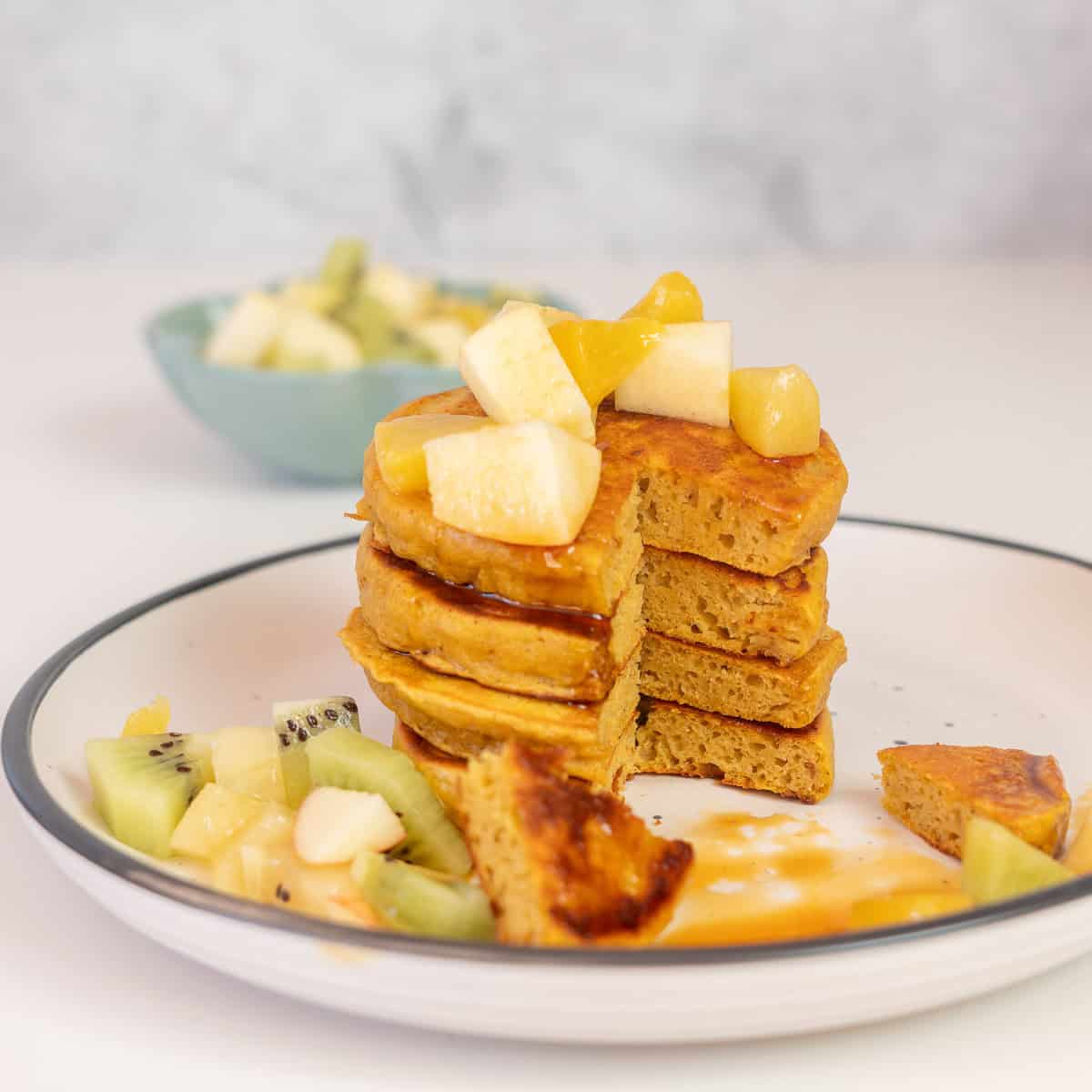 A stack of pancakes on a plate with a triangular wedge removed from the stack to show the fluffy inside of the pancakes. 