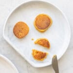A grey silicone baby plate with 3 small pumpkin pancakes on it and a small baby knife.