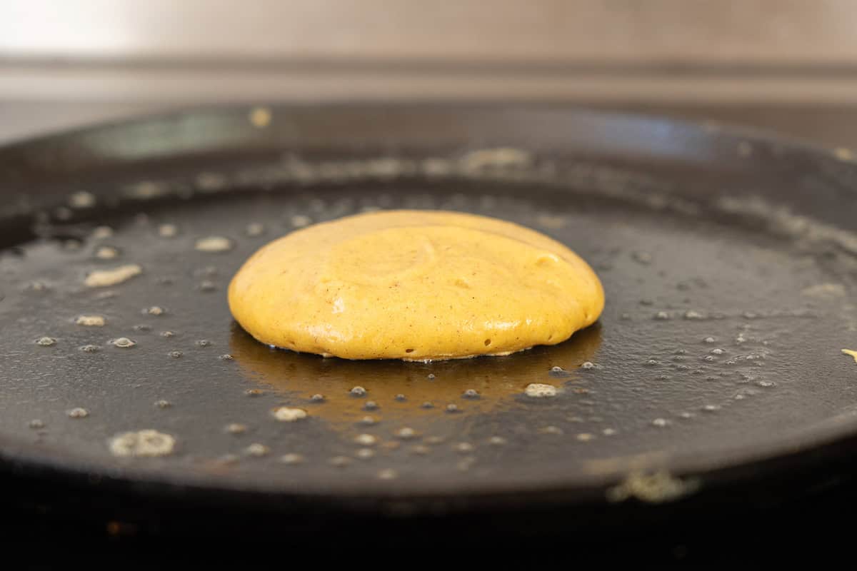 A small pumpkin pancake cooking on a cast iron skillet. 