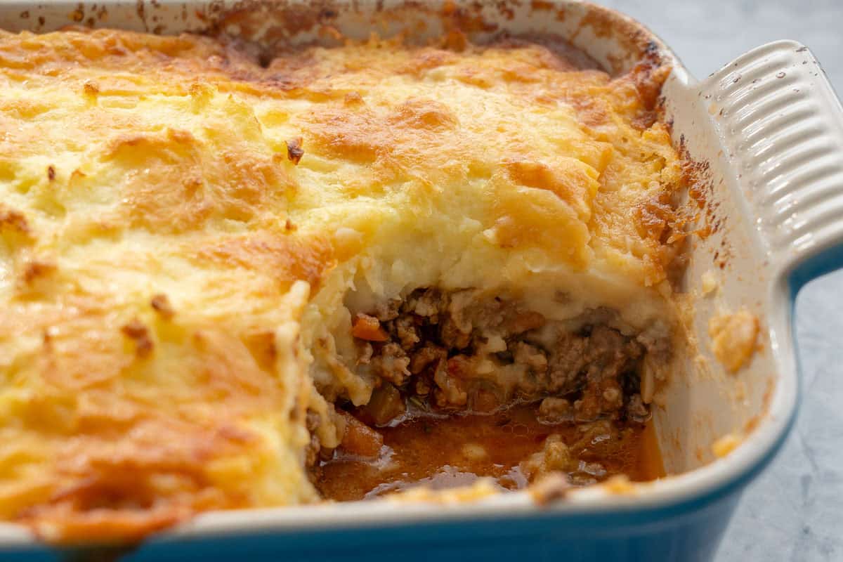 Close up of pie in baking dish with corner scooped out so you can see the mince and potato cheese layers.