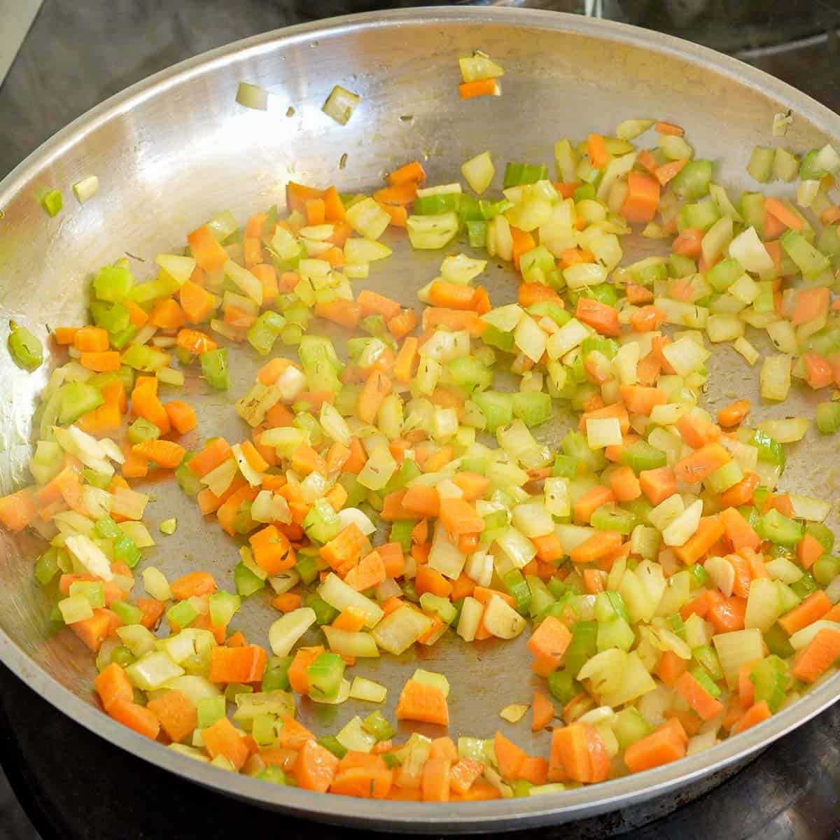 Carrot, celery, onion with herbs and garlic sautée in pan.