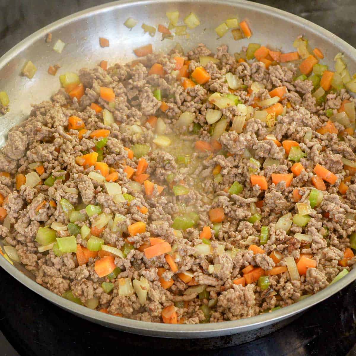 Mince cooking in pan with sautéed carrot, celery, onion with herbs and garlic.