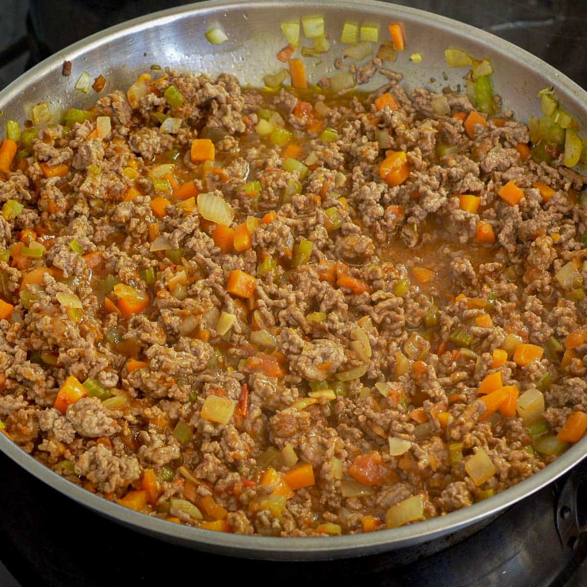 Stock and tomato relish simmering in pan with mince, carrot, celery, onion with herbs and garlic.