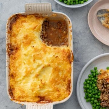 Shepherds pie in baking dish with corner scooped out and placed on dinner plate with serve of peas.