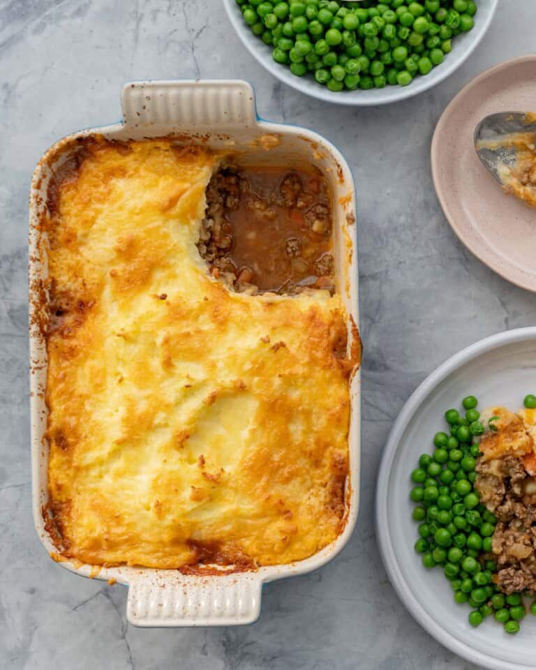 Shepherds pie in baking dish with corner scooped out and placed on dinner plate with serve of peas.