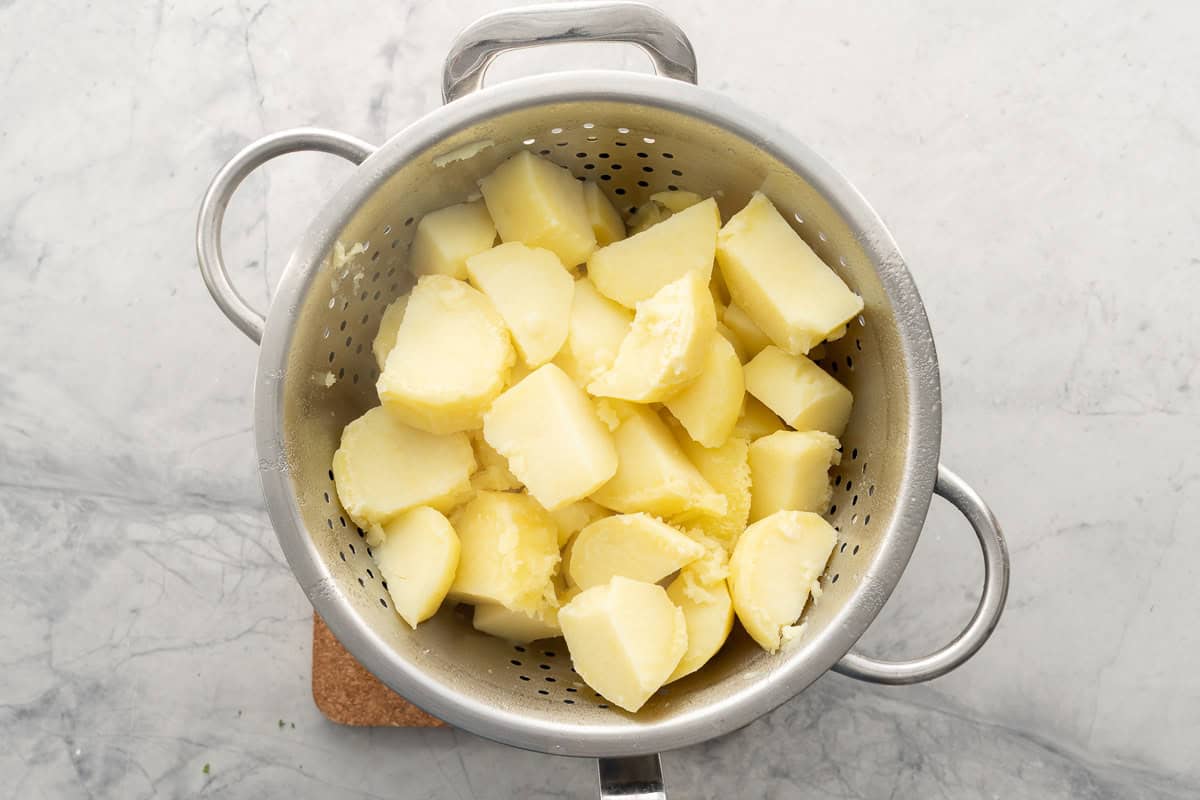 Boiled chopped potatoes in colander.