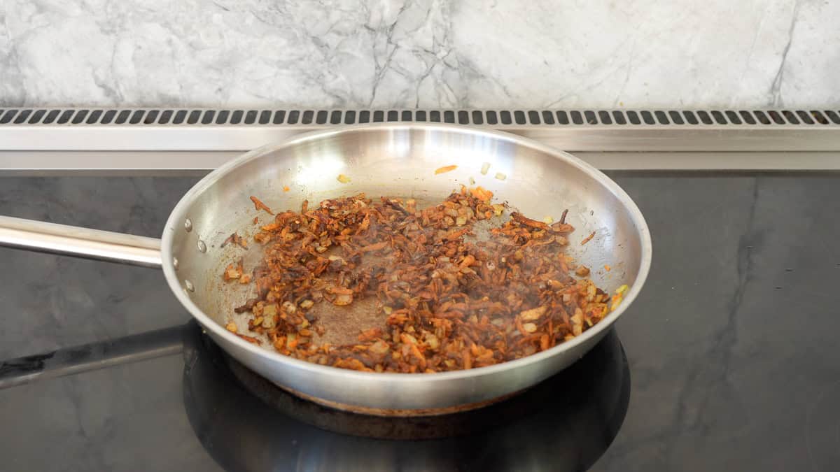 Sautéed grated carrots, diced onions and spices in a stainless steel fry pan.