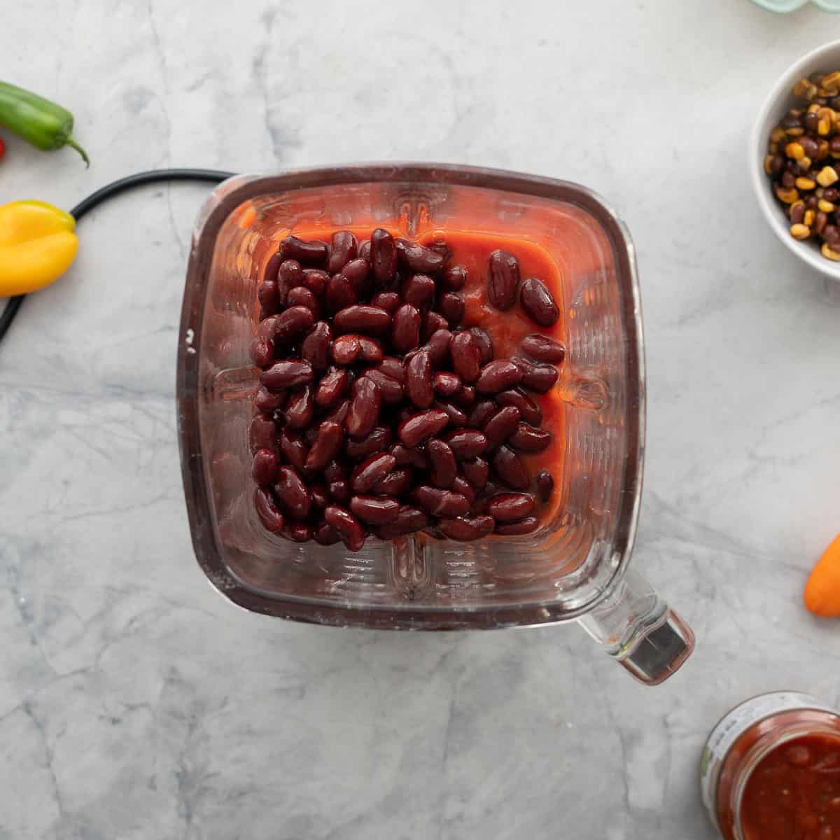 A glass blender jug with tinned tomatoes and red kidney beans visible.