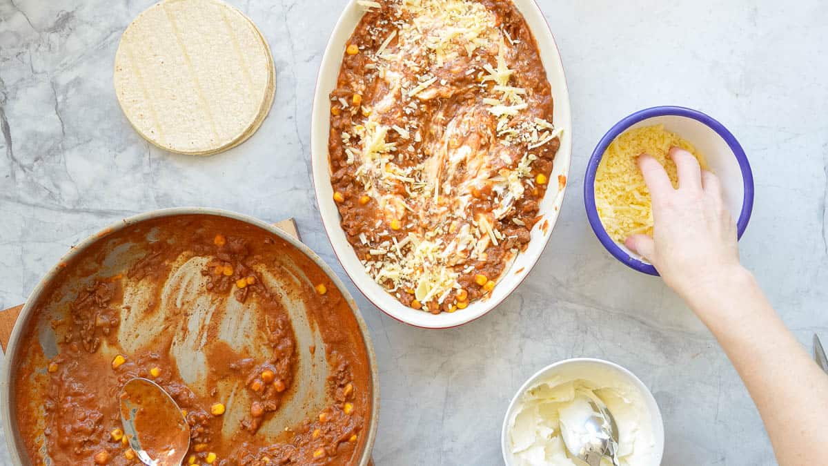 A Mexican lasagne being assembled into an oval baking dish.