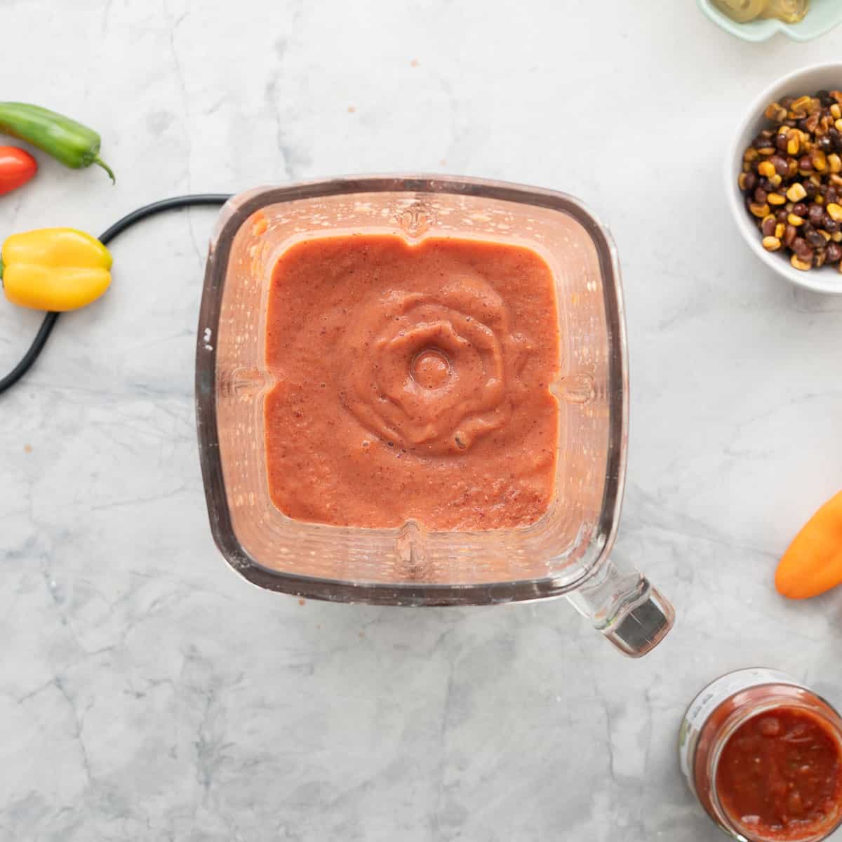 A glass blender jug filled with a pale red smoothie of beans and tomatoes.