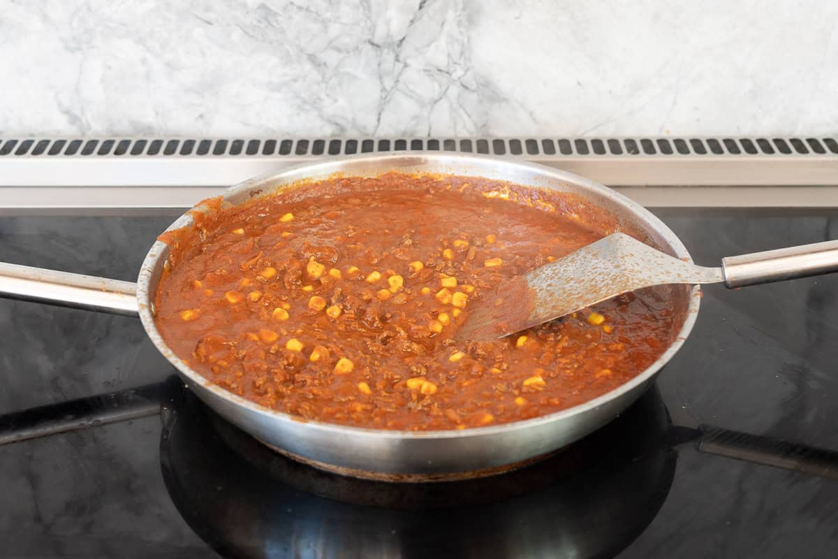 Large stainless steel fry pan on an inducitno stove top filled with saucy mexican mince.