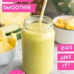 Tropical smoothie in tall glass with straw, chopped pineapple in bowl and whole pineapple blurred in background. With text overlay: Tropical Smoothie Kids Love It!.