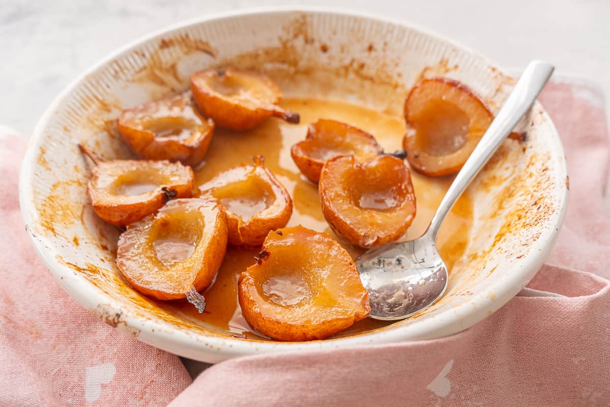 Baked pears caramelised in baking dish with serving spoon.