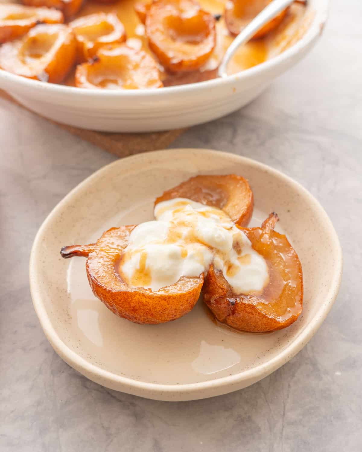 Three caramelised baked pears served on a plate with greek yogurt and a drizzle of maple syrup on top.