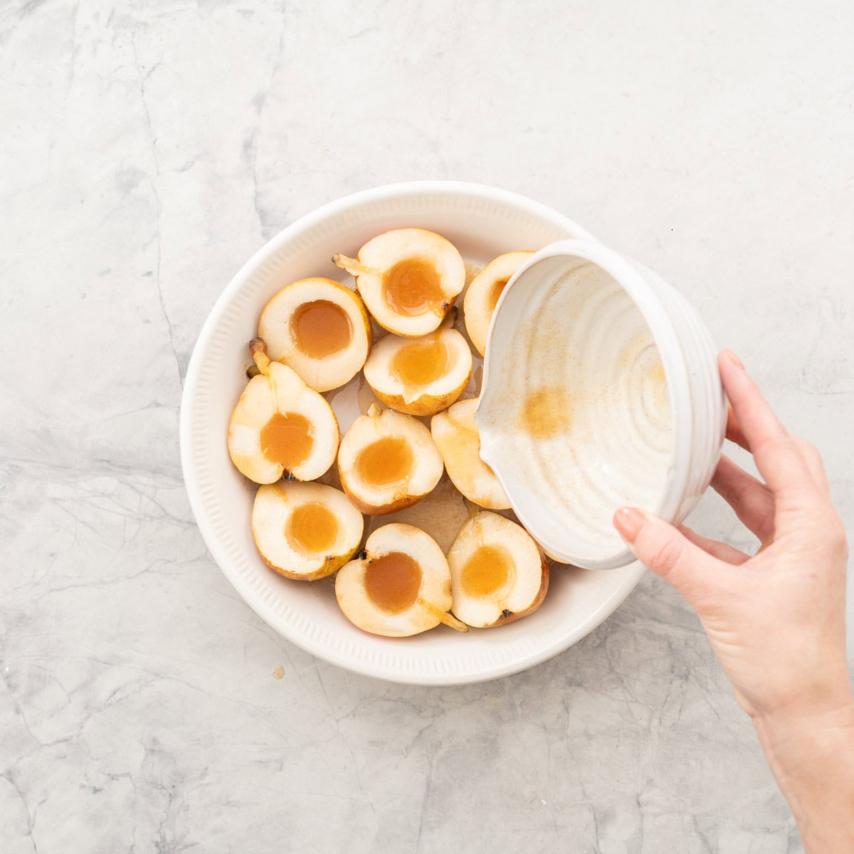 Bowl of wet ingredients being poured evenly on top of pear halves.