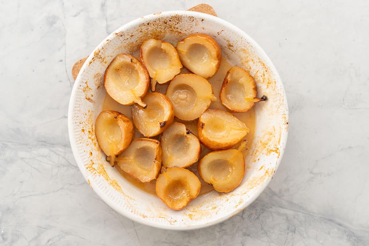 Glossy juicy baked pears skin side down in baking dish.