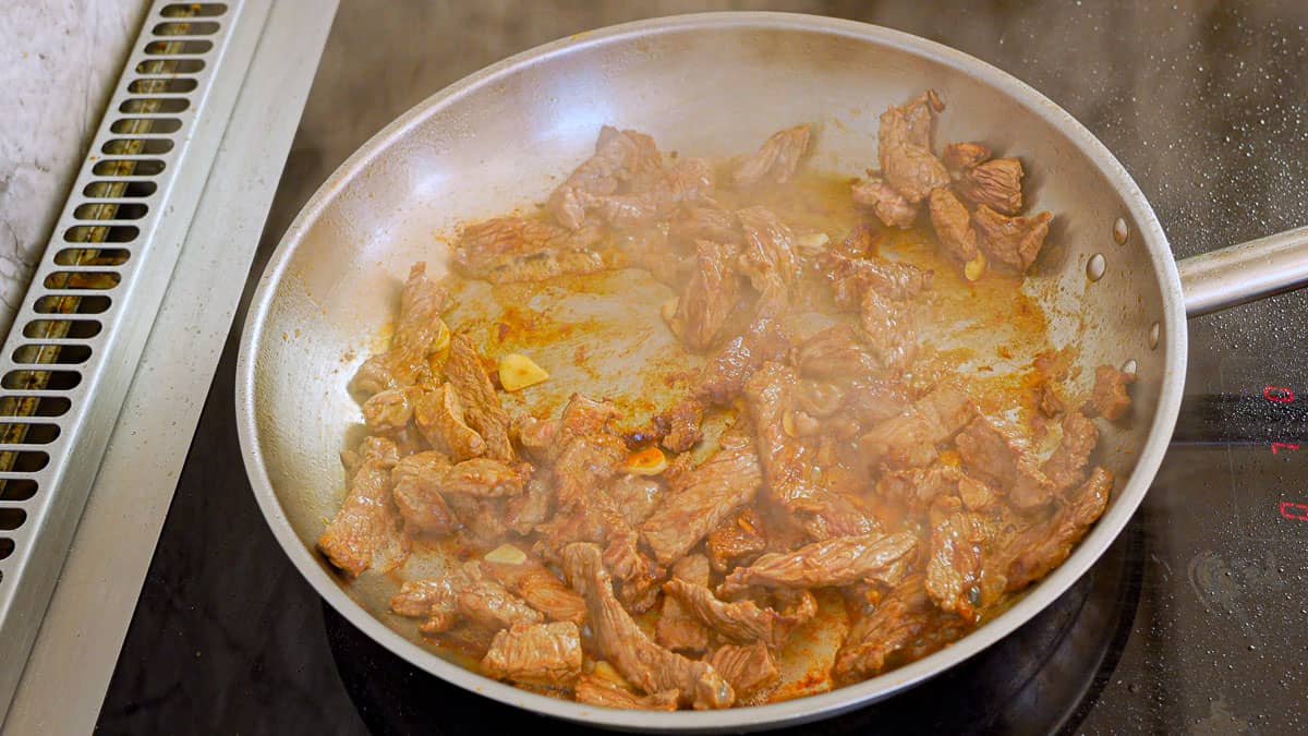 Strips of browned beef in a stainless steel skillet.