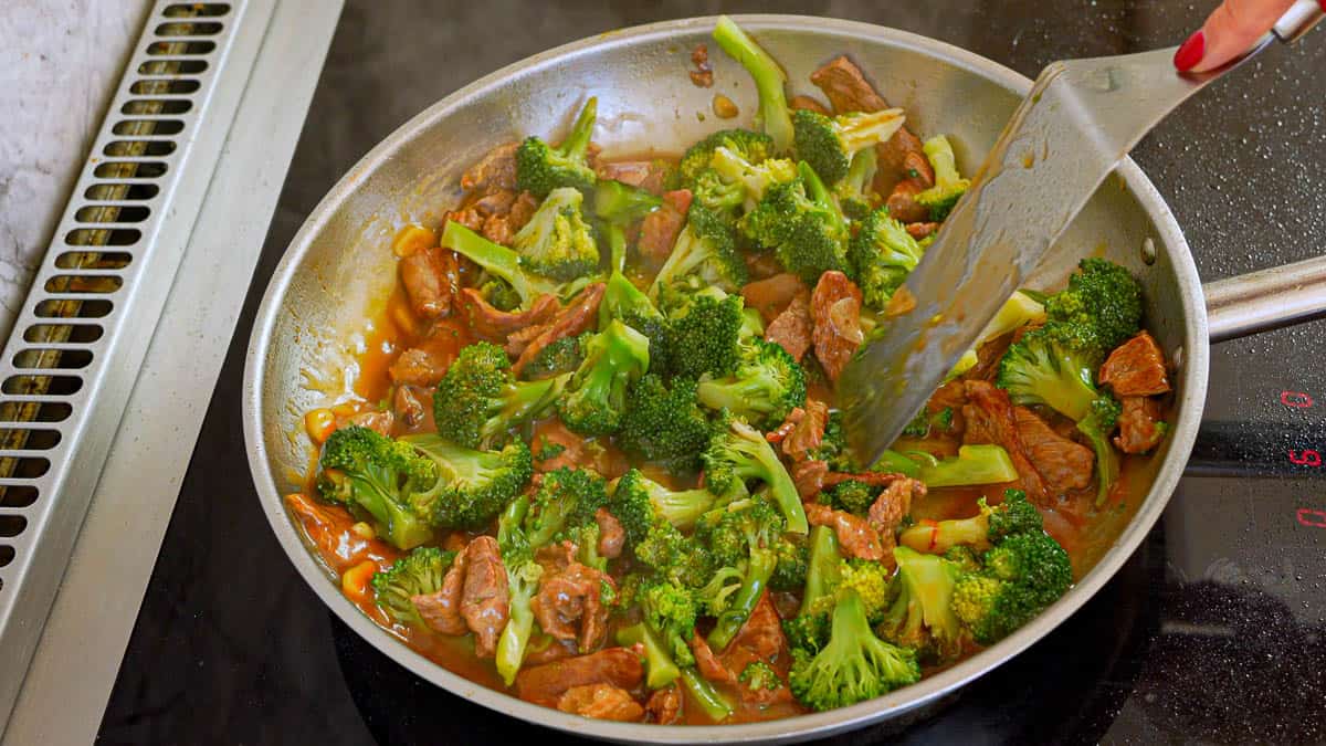 Green florets of broccoli being stirred through a saucy beef stir fry. 