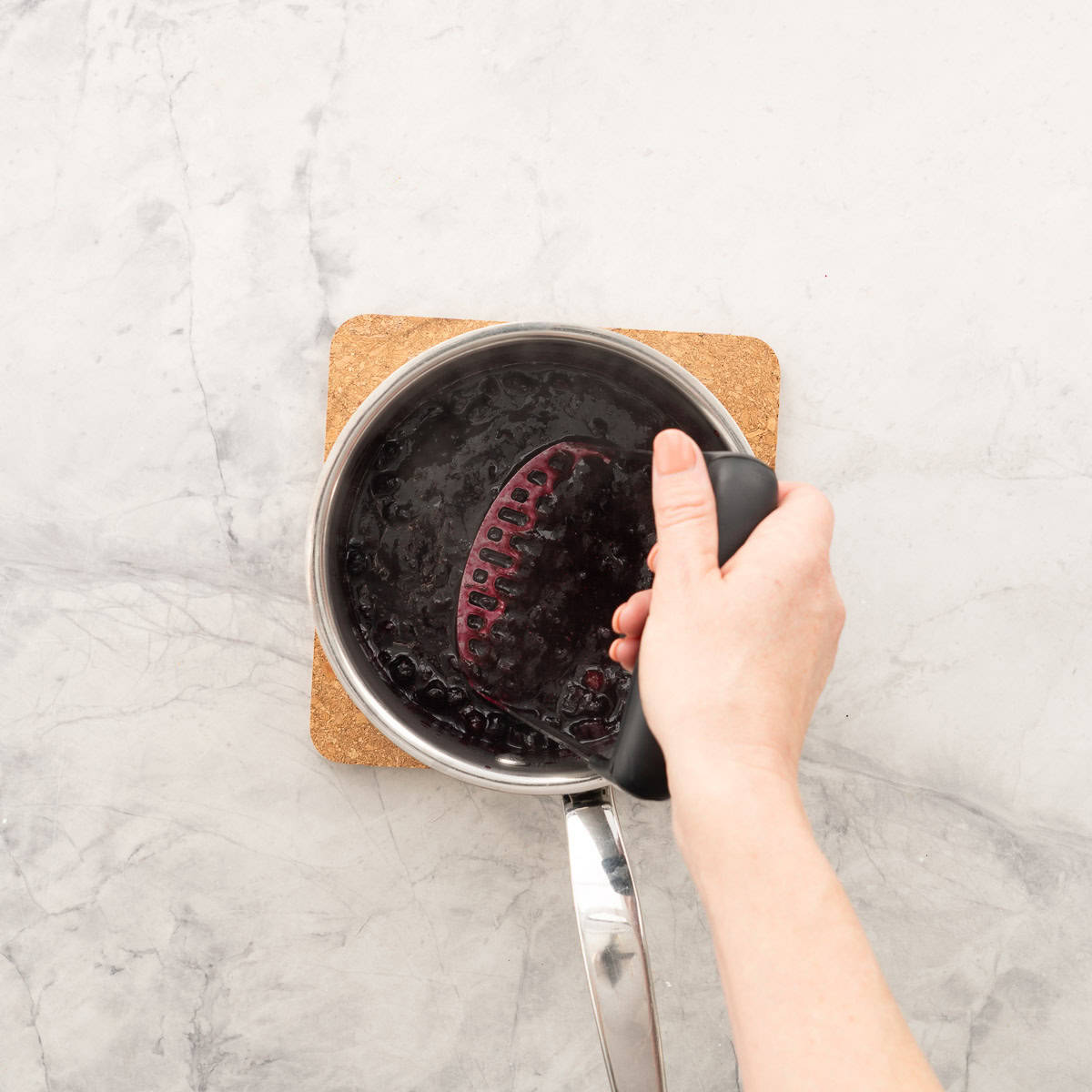 Blueberry chia jam in a pot being mashed with potato masher.