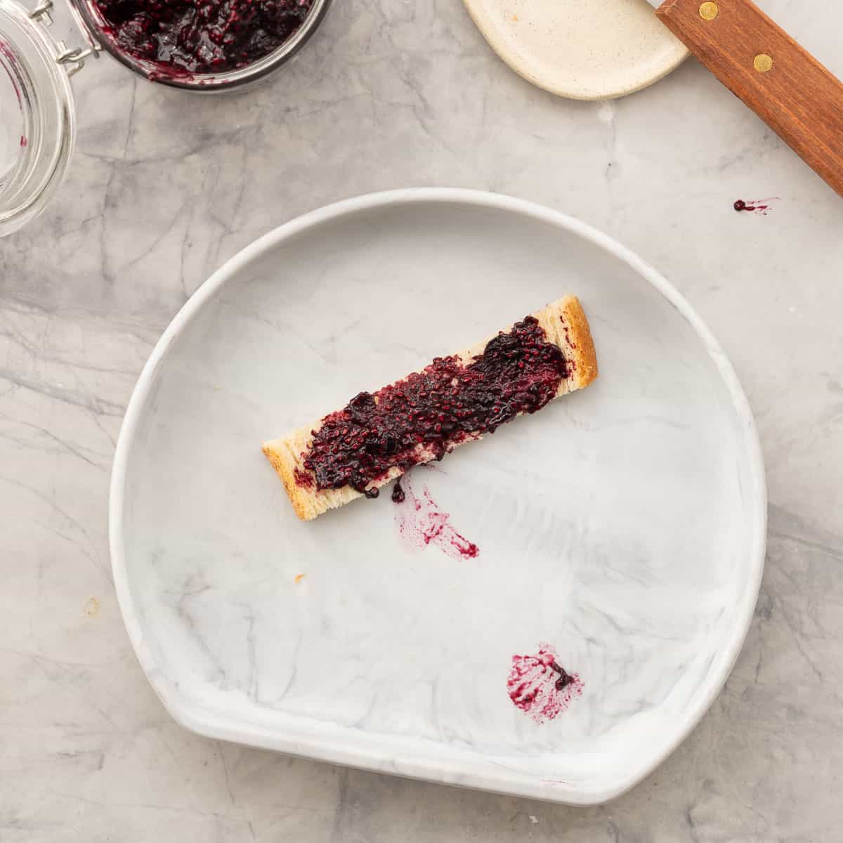 Blueberry chia jam spread onto slice of bread, on children's silicone plate.