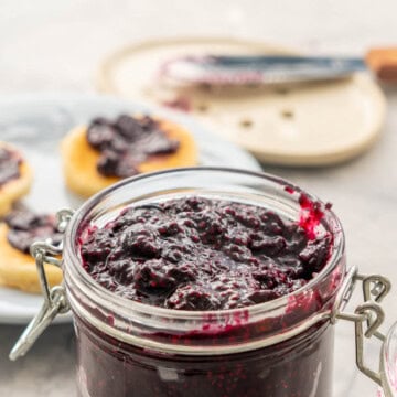 Chia Blueberry jam in jar with lid open filled to the top, in background a plate mini pancakes with jam spread on them.