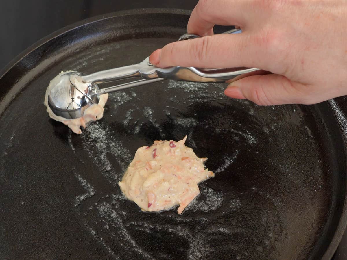 Carrot cake pancake batter being scooped into pan with cookie scooper.