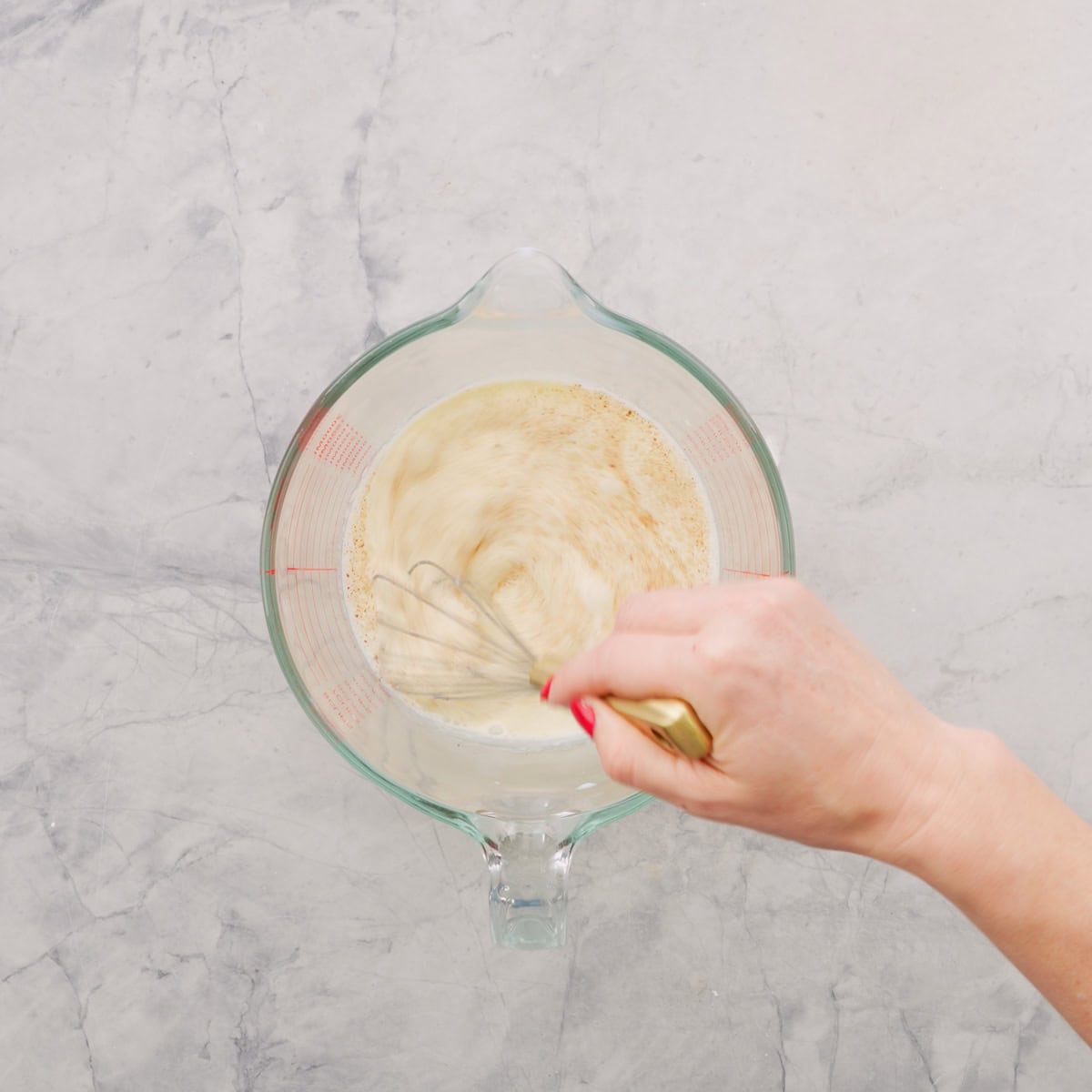 Milk and spices being whisked in a glass mixing jug. 