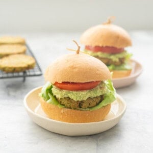 Burger on a plate with lettuce, chickpea patty, guacamole, slice of tomato and top of burger.