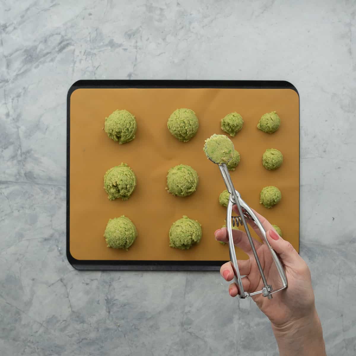 Hand holding a cookie scoop with chickpea pattymixture inside and scoops on baking tray.